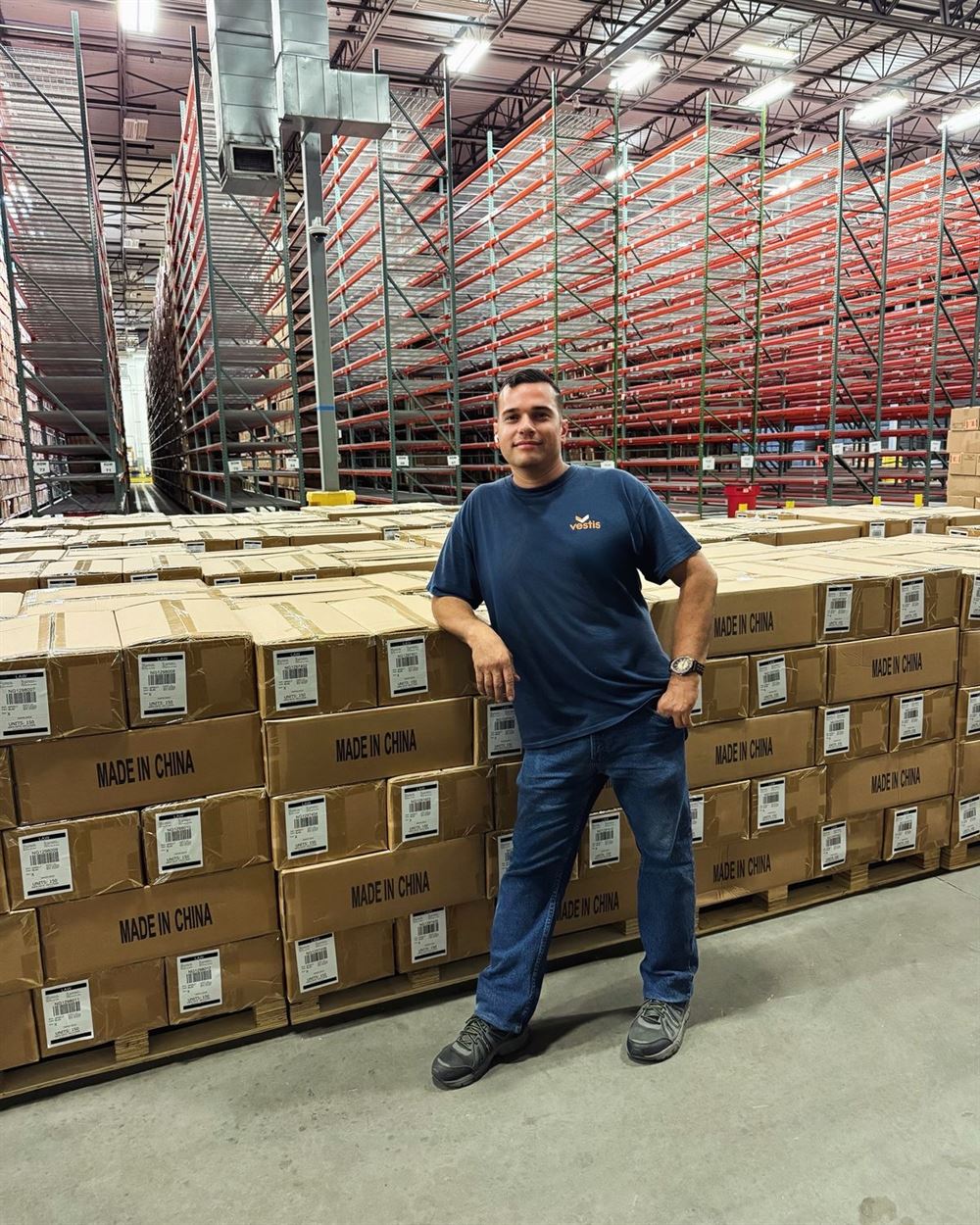 A Skysprint team member stands in front of rows of labeled boxes, with tall orange racking behind him.