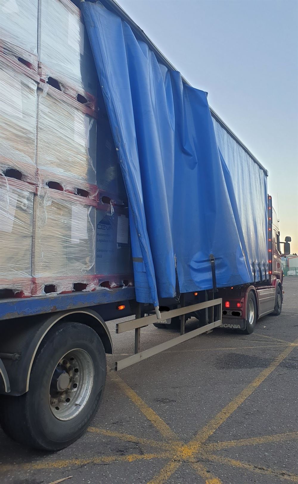 A curtain-side trailer opened to show shrink-wrapped pallets strapped in place.